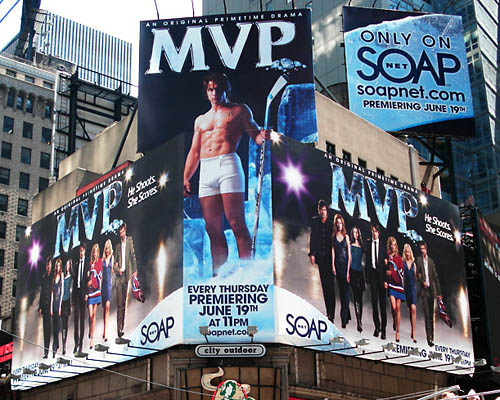 Billboards for â€˜MVP' cover two sides of a Times Square building, with tall billboard attached square on the corner showing a shirtless guy with a hockey stick