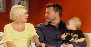 Blond Tori Spelling looks at her husband, Dean Whatever, as he holds a baby